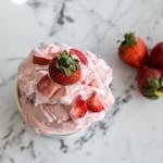 A bowl of homemade strawberry ice cream with fresh strawberries on a marble countertop.