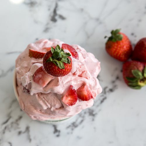 A bowl of homemade strawberry ice cream with fresh strawberries on a marble countertop.