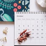 Flat lay of an October calendar and planner with autumn leaves and coffee cup, perfect for planning enthusiasts.