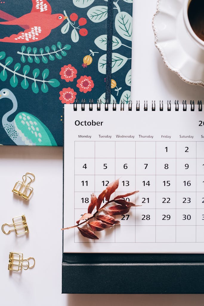 Flat lay of an October calendar and planner with autumn leaves and coffee cup, perfect for planning enthusiasts.
