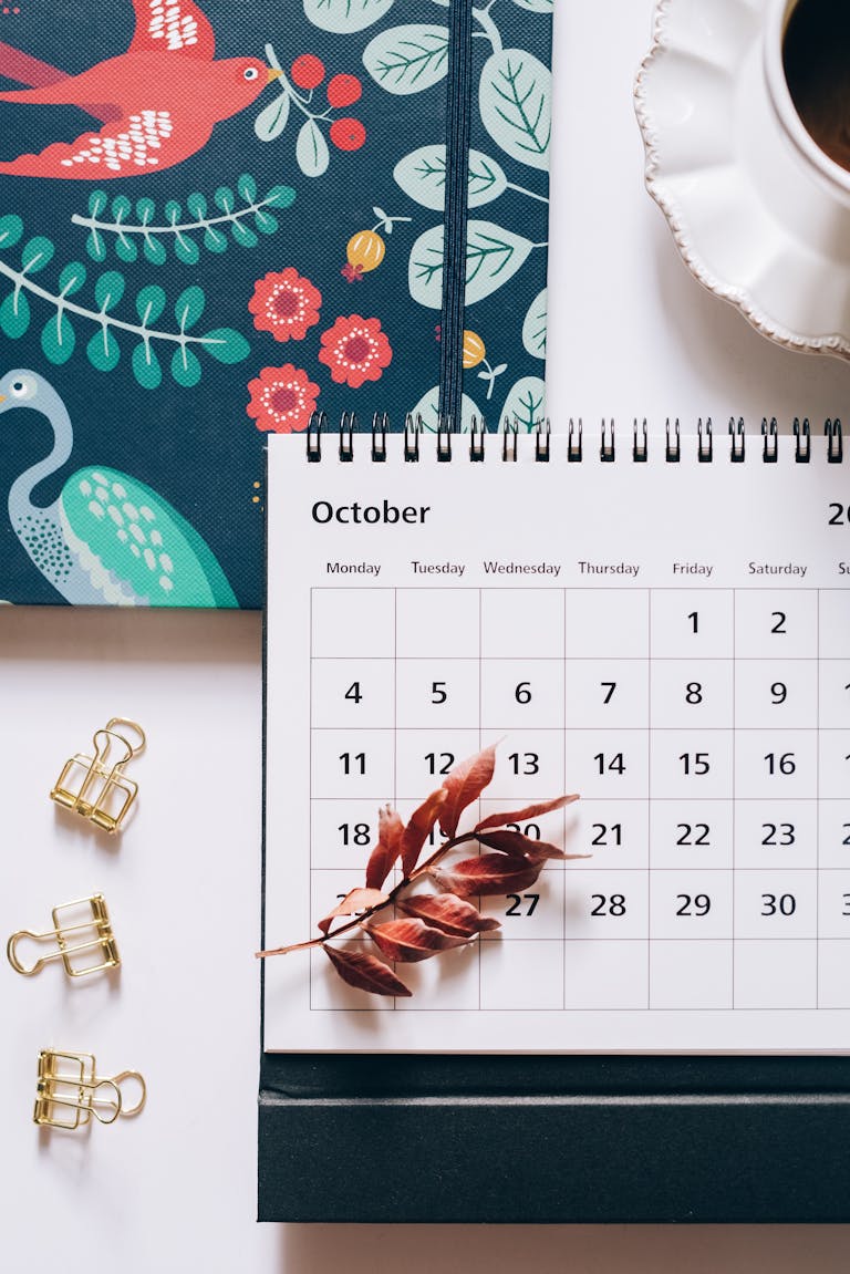 Flat lay of an October calendar and planner with autumn leaves and coffee cup, perfect for planning enthusiasts.