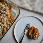 Whole roasted sweet potato topped with toasted marshmallows and chopped pecans