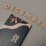 A 2025 planner displayed with wooden letters spelling 'December' on a neutral background.