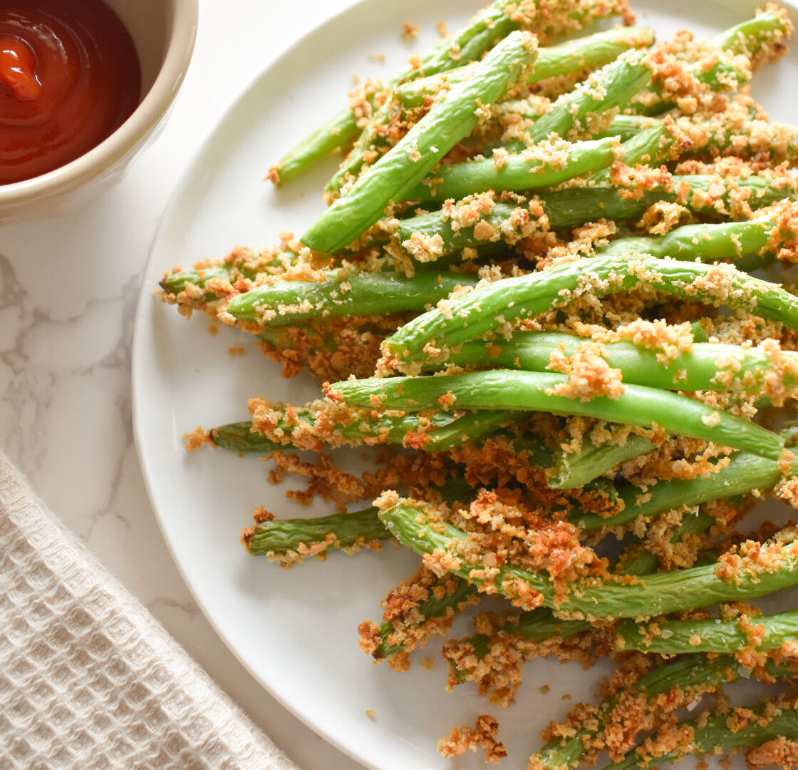 Golden brown green beans in air fryer basket.