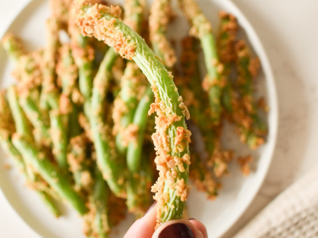 Crispy air fryer green beans on a white plate with lemon wedges.