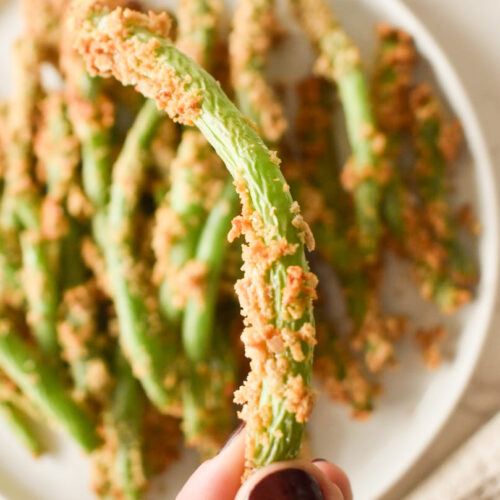 Crispy air fryer green beans on a white plate with lemon wedges.