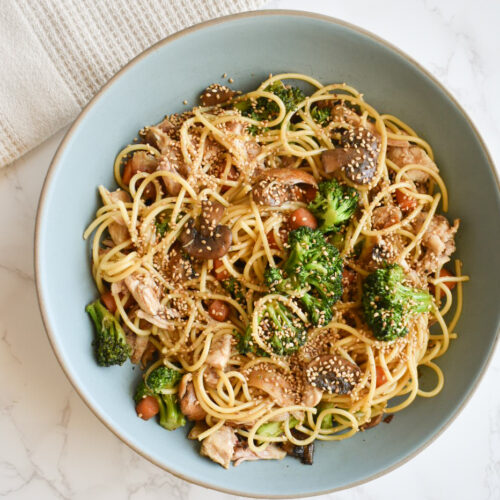 Close-up of sesame chicken pasta with vegetables and sesame seeds