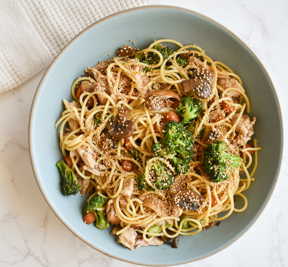 Close-up of sesame chicken pasta with vegetables and sesame seeds