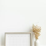 A minimalist setup featuring a framed calendar and decorative vase against a white background.