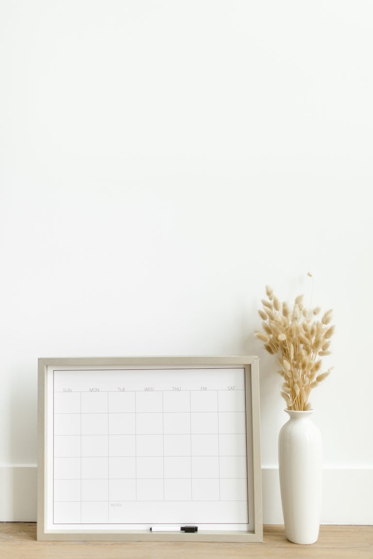 A minimalist setup featuring a framed calendar and decorative vase against a white background.