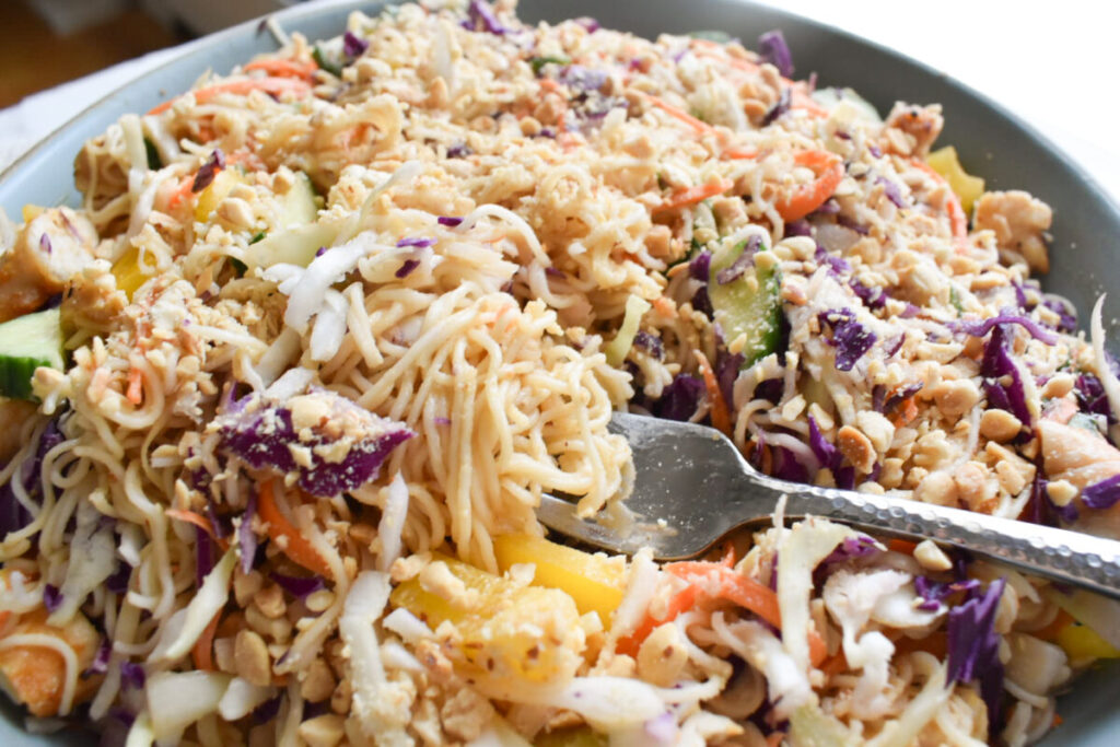 Close-up of peanut dressing being poured over ramen salad