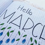 Open notebook with "Hello March" illustration featuring colorful raindrops and leaves.