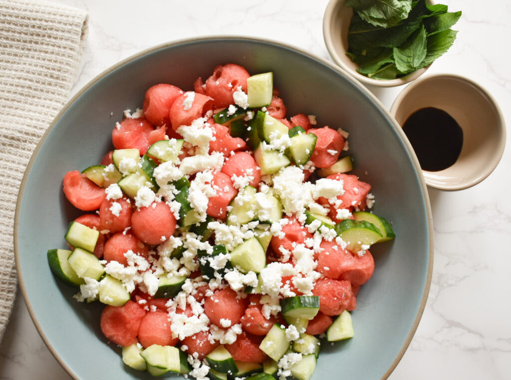 Watermelon Ball Salad with cucumber, feta, mint and balsamic glaze in a white serving bowl