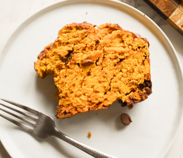 A slice of pumpkin chocolate chip bread served on a plate with a warm cup of coffee.